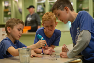 Three boys use a 3D printing pen to create a small art piece.