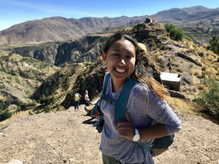 Olivera smiles on a hike with mountains in the background.