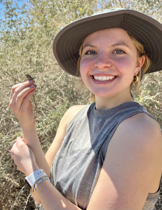 Layne smiles at the camera holding a small lizard.