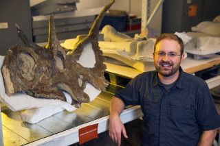 Randy Irmis stands for a portrait next to a ceratopsian skull in the NHMU paleontology collections. 