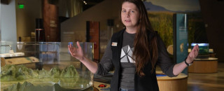 An NHMU educator stands in the Great Salt Lake gallery wearing a vest