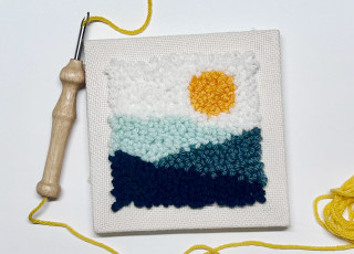 A punch needle embroidery piece with a mountain landscape and a sun.