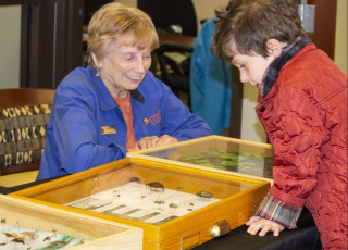 A museum volunteer shows a kid museum specimens at an event.