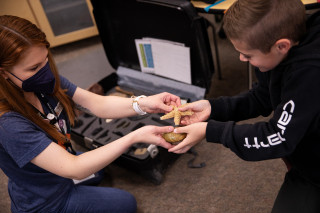 An NHMU educator hands items to a student