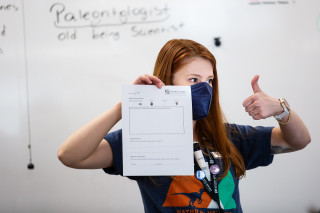 A museum on the move educator, wearing a blue mask, holds up an example worksheet