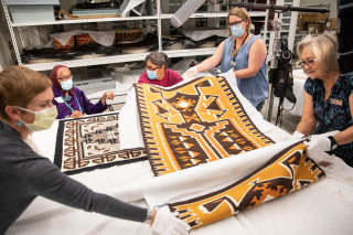 Museum staff roll out a Navajo rug for inspection by a weaver.
