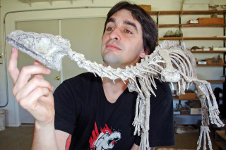 Dr. Antoine Bercovici poses for a photos with a dinosaur fossil.