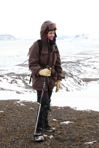A scientist in a large coat stands on a ridge in a frozen landscape. 