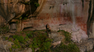 Ella sits on a rock outcrop in a jungle. 