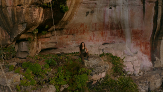 Ella sits on a rock outcrop in a jungle.