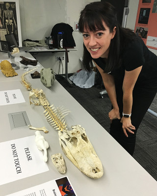 A paleontologist stands over a small skeleton on a tabletop. 