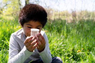 A boy looks at a bug in a jar. 