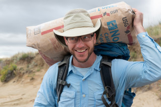A man carries a large bag of plaster on his shoulders.