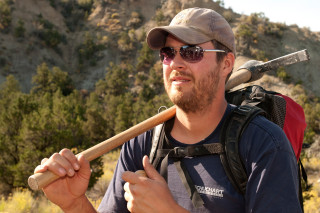 A paleontologist with a pick axe resting on his shoulder. 