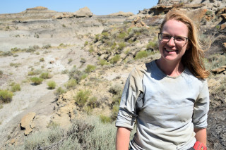A woman smiles for the camera while standing in badlands. 
