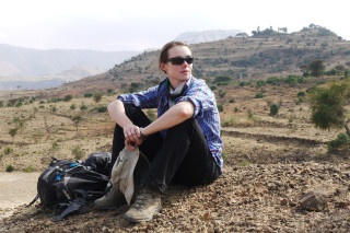 A paleontologist sits on a ridge to rest. 