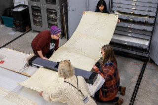 Collections staff feed a large map through the scanner.
