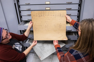 Collections staff remove a historic, hand written document from a drawer at NHMU.