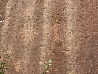 Photo of rock art in Range Creek Canyon. Close up of rocky face with art etched in. A human figure and what looks like the sun are painted on the rock.