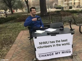 Male volunteer at table with sign that says &quot;NHMU has the best volunteers in the world.&quot;