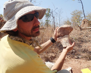 A paleontologist holds up part of a fossil while working in the field. 