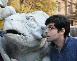 A paleontologist poses for a photo next to a dinosaur statue. 