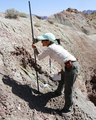 A paleontologist takes a measurement while standing in badlands. 