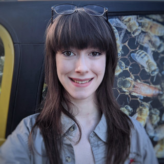 Jenna smiles at the camera in front of a car with honeybees picture on the side.