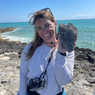 Molly smiles holding a large rock in front of a big lake.