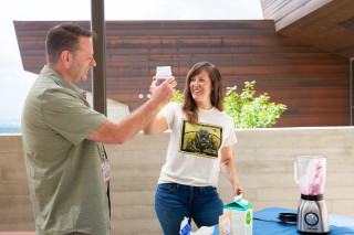 A man and woman toast with glasses while standing outside. 