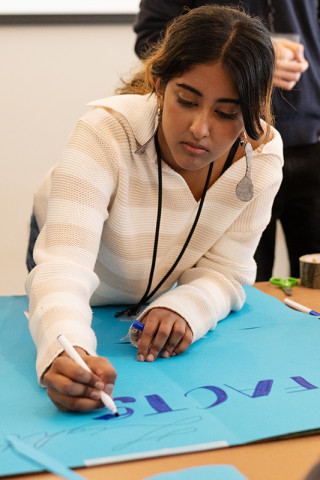 A young woman draws on a poster board. 