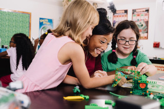 Two girl scouts and a girl scout leader build a small machine with connectable bricks.
