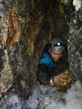 Dr. Tyler Faith, chief curator of NHMU, squeezes through the narrow opening of an undisclosed cave.