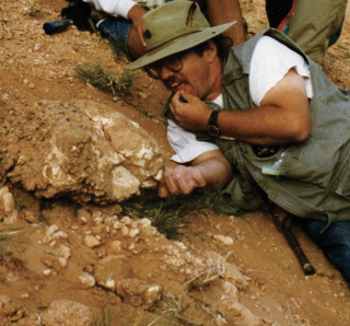Dr. Jim Kirkland crouches next to a fossil bed on a mountain.