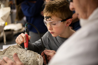 A boy uses an air scribe to chisel away rock.