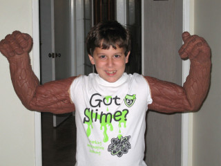 A young boy wears costume muscular arms. 