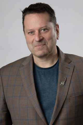 A picture of a man in a grey shirt and brown jacket