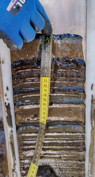 A person uses a tape measure to measure a core sample.