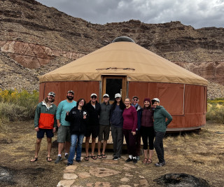 A group of people in coats in front of a yurt with desert cliffs in the background