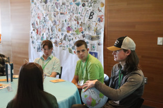 A group of teens sits at a table while one of them holds a globe ball