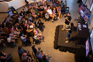 A crowd of people gathers around a stage with two BugFest presenters