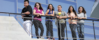 Students stand at a railing in front of a museum. 