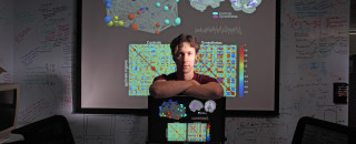 A portrait of David Eagleman standing before a projection of the human brain.
