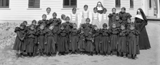 A group photo of young students in formal dress outside the school
