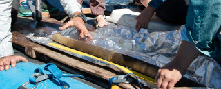 Scientist on a raft examine a tube-shaped lake core pulled from the lake bed. 