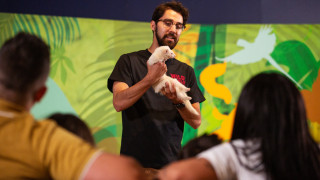 A host holds a ferret before a watching family in the exhibit. 