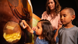 A young girls plays with an interactive in the exhibit as her family watches. 