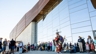 An indigenous dancer performs for an audience gathered outside NHMU.