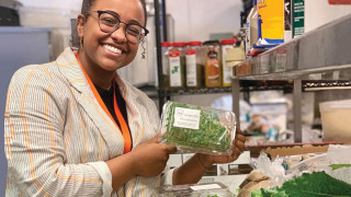 A woman holds up a package of greens and smiles for the camera.