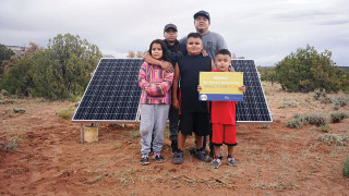 A family stands before a solar panel.